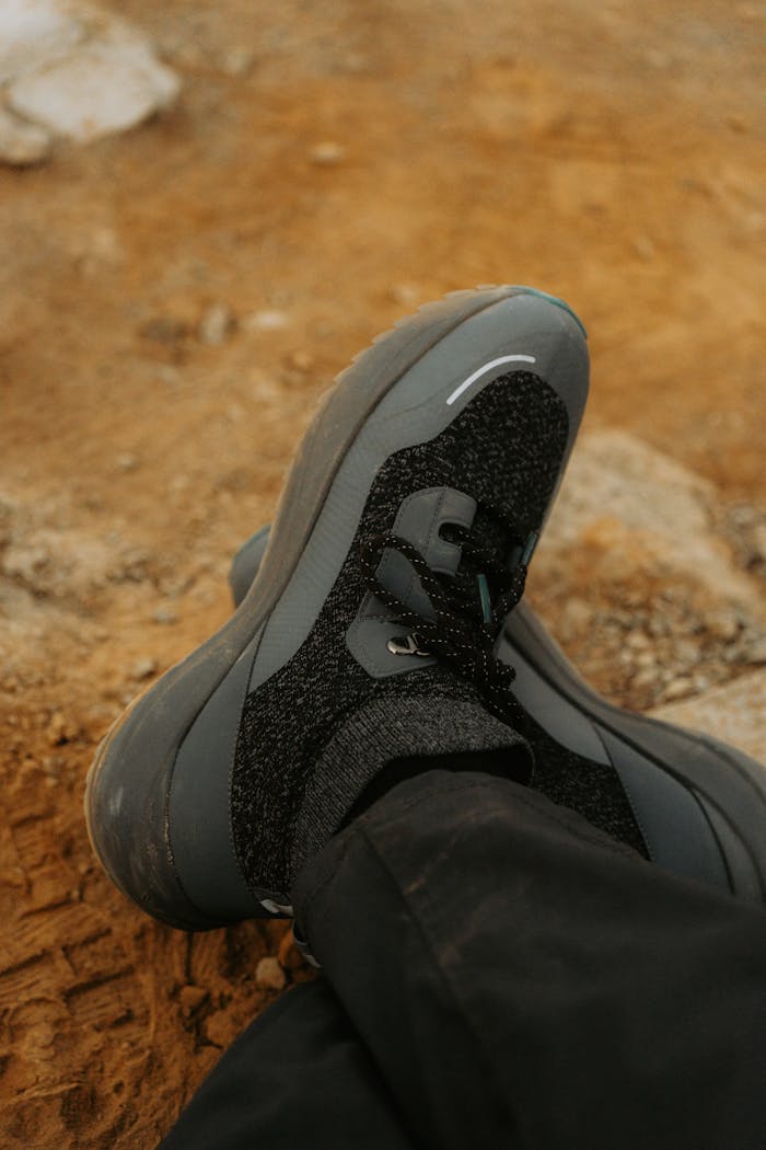 Man's foot in casual sneakers resting on dusty outdoor terrain, showcasing footwear style.